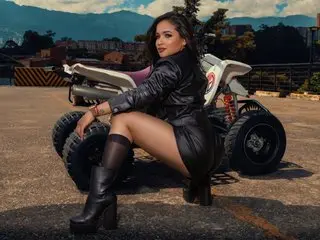 Celene_Ortiz poses nakedly in a black leather outfit, sitting on a white ATV against a scenic outdoor landscape.