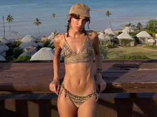 Celines_Dream_x poses in a patterned bikini top and bottom, showing her bare stomach and chest while standing outdoors near a wooden railing.