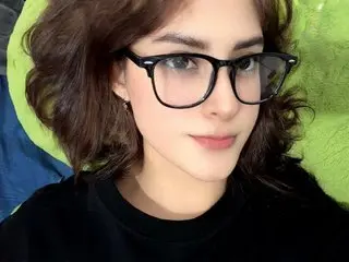 ChaeyoungDe poses with a close-up headshot, showing her dark wavy hair and black-rimmed glasses while wearing a black top.