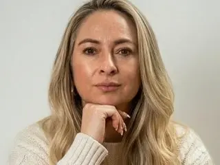 ChanelGold79 poses with a hand under her chin, showing her blonde hair and face against a plain white background.