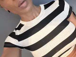 Woman in a black and white striped crop top posing against a grey wall in a casual mood.