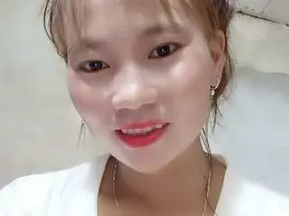 Chani_bae smiles close-up, showing her face, hair, and gold earrings while wearing a white top.