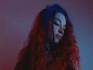 CharickAddler poses with her long, curly red hair partially covering her face against a plain dark background.