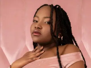 Young woman with long black braids wearing a pink velvet top against a soft pink background.
