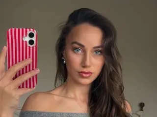 CheekySabrina poses for a selfie, showing her face and long brown hair against a plain background.