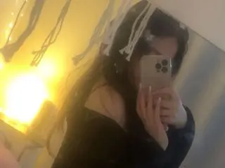 Cherryrosealiee poses for a mirror selfie, showing her long dark hair and a black top against a warm, lit background.