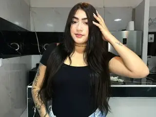 ChloeHills19 with long dark hair and tattoos wearing a black tank top and choker in a kitchen setting.
