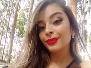 ChloeMackenziee with long brown hair and red lipstick, looking directly at the camera in a bright outdoor setting.