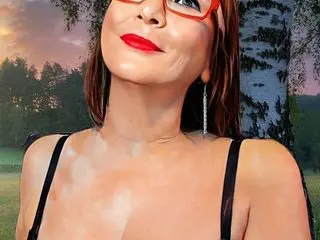 Smiling woman in red glasses and black tank top posing outdoors against a sunset forest background.