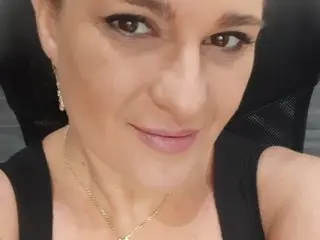 Claraboobies looks directly at the camera with a slight smile, wearing a black tank top and a gold necklace.