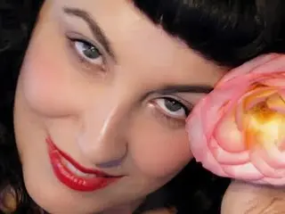 Claudine smiles close-up, showing her dark hair and red lipstick against a dark background.