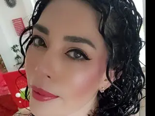 Woman with curly black hair and winged eyeliner posing with a soft, glamorous makeup look indoors.