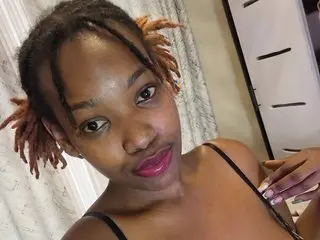 Coco_bliss smiles at the camera while wearing a black strap top in her bedroom.