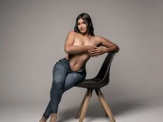 CorinaBrown poses naked while sitting on a black chair, resting her hands on her bare breasts.