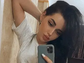 Young woman with long dark hair in a grey t-shirt taking a moody selfie in a bright room.