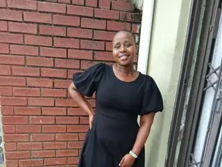 CreamyCurvesx smiling in a black dress while posing outdoors against a red brick wall.