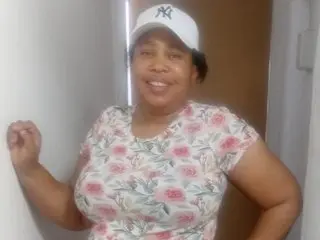 Smiling woman in a floral print shirt and white baseball cap posing indoors with a happy mood.