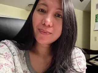 CreamyyLipss69 — CreamyyLipss69 smiles for a selfie while wearing a white floral patterned shirt in her room.
