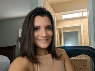 Smiling brunette woman in a beige sleeveless top relaxing in a bright modern bedroom.