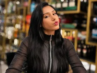 CristalMontiel poses with a pouty expression, wearing a black long-sleeved mesh top with her long dark hair down in a warm indoor setting.