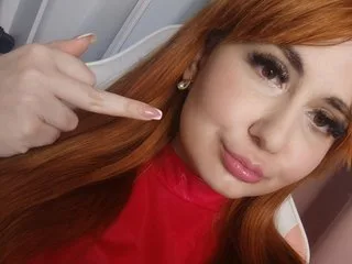 CruelSiren poses with a hand to her chin, showing her long red hair and light eyes.