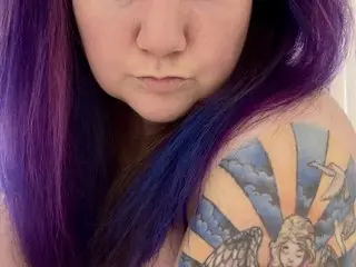 CrystalRivers33 shows her purple-tinted hair and a large, colorful sun tattoo on her shoulder and upper arm.