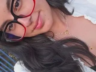 Crystal_Moom smiles at the camera wearing red glasses and a pearl necklace with her long black hair flowing over her shoulders.