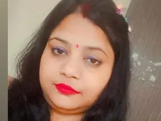 Portrait of a woman with red lipstick and bindi looking calmly at the camera in a soft indoor setting.