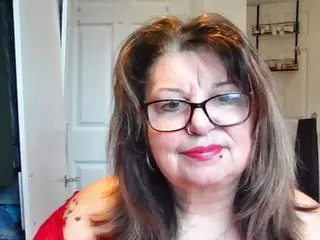 CurvyCougarBecca poses with long brown hair and glasses, wearing a red top while looking directly at the camera in an indoor setting.