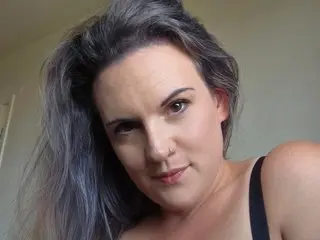 CurvyMaskedBabe looks into the camera with her long grey hair flowing over her shoulder in a close-up selfie.