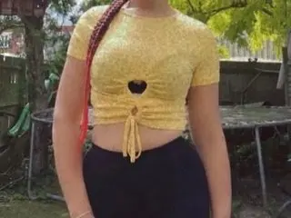 CurvyShannel poses in a yellow lace crop top that shows her midriff and cleavage, standing outdoors against a soft green background.