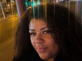 CurvySiennaxx — CurvySiennaxx poses with a soft smile, showing her dark curly hair and clear skin in a close-up shot.
