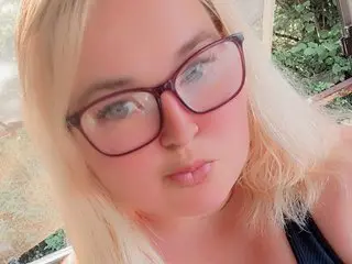 CurvySweetMaya looks into the camera with a close-up view of her face and blonde hair, wearing dark-rimmed glasses.