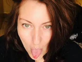 Curvygirllouisa licks her lips with a playful expression, showing her face and long brown hair in a close-up shot.