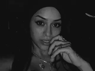 Moody black and white portrait of a woman with dark hair and silver jewelry in a low-light setting.