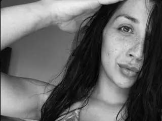 Dani_Angel poses with her hand in her dark hair, showing her bare shoulders and face in a close-up black and white shot.