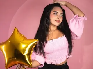 Danivelvet30 poses with long black hair and a pink off-the-shoulder top against a pink background, holding a large gold star balloon.