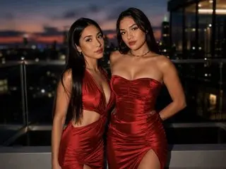 Danna3333 poses in a red satin dress with a deep neckline against a dark city skyline at night.