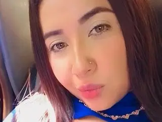 DannaHot25 looks at the camera with long brown hair and a blue top, showing her face and shoulders in a close-up shot.