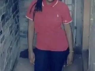 DarkCherryx25 wears a red short-sleeved polo shirt and dark pants while standing in a hallway with brick walls.