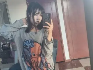 DarkMoon_66 poses for a mirror selfie wearing a grey long-sleeved graphic t-shirt with her hands near her face.