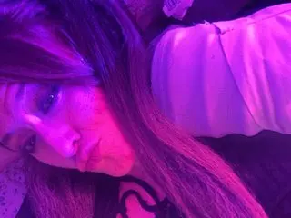Darnette_Daisy poses with a close-up view of her face and long dark hair, lit with a purple glow.