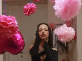 Glamorous woman in a black cutout outfit surrounded by pink paper flower decorations in a festive room.