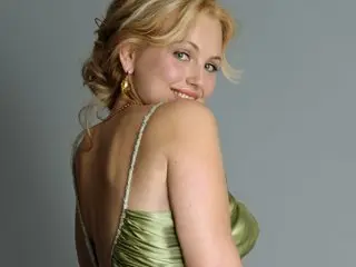DeliciousAlbany poses looking over her shoulder, showing her blonde hair and wearing a light green satin camisole or slip dress.