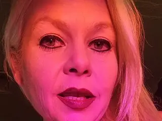 Close-up portrait of a blonde woman with dramatic dark eyeliner and red lipstick in warm pink lighting.