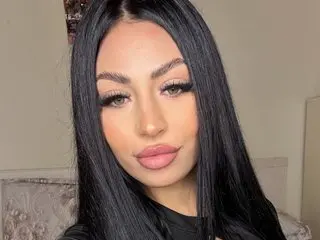 DelilahRayn poses for a close-up selfie, showing her long black hair and pink lipstick against a plain background.