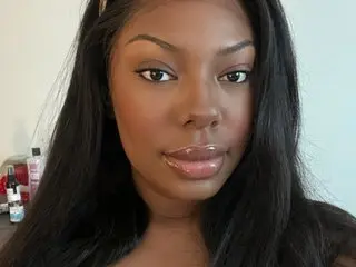 Close-up portrait of a beautiful Black woman with long dark hair and glowing makeup in a bright indoor setting.
