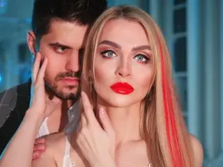 DenLina poses with her hands near her face, showing her long blonde hair and red lipstick in a close-up shot.