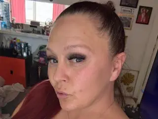 Destiny_Rabbit pouts her lips in a close-up selfie, showing her face and pulled-back hair against a room background.