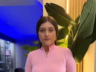 Devon_Carter poses with a direct gaze, wearing a pink long-sleeved mock-neck top with her dark hair styled straight down.